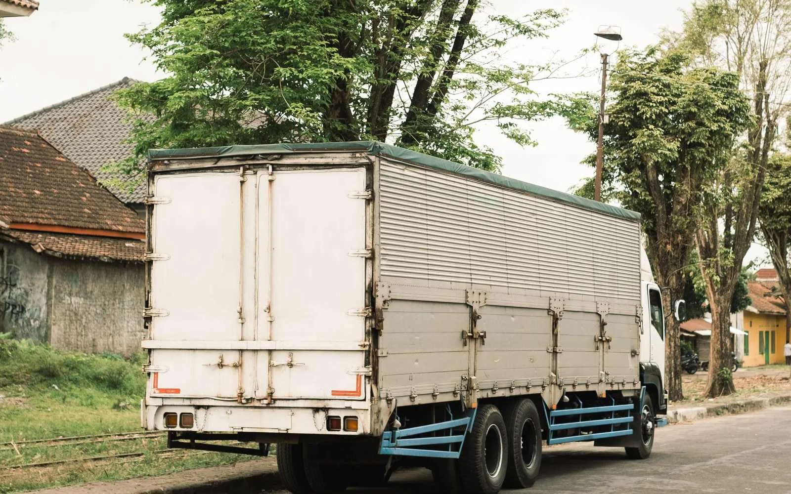 Large box lorry parked at ground level on a tree-lined road